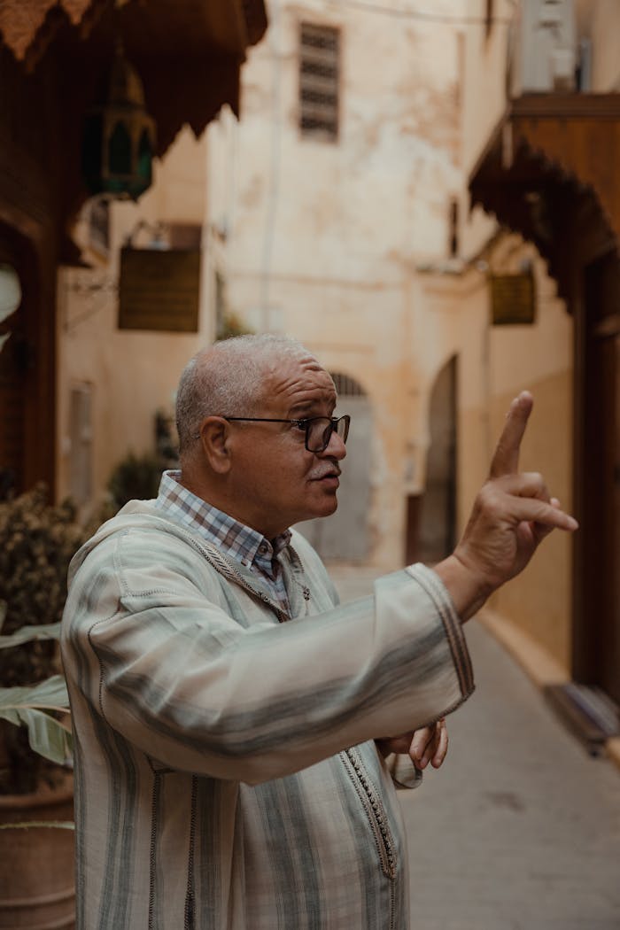 services-04 An adult man with glasses gestures while speaking in a historic street.