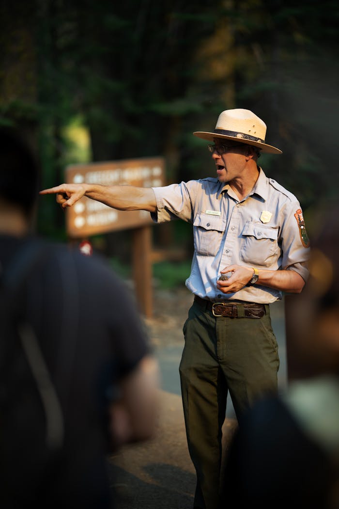 Park ranger guiding a group through a forest area, pointing with emphasis.